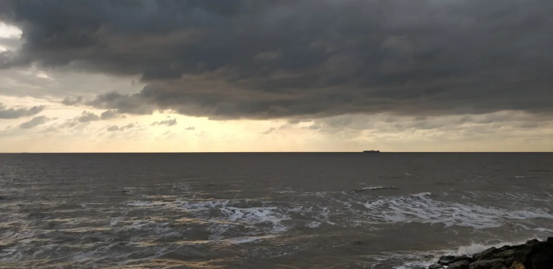 Photograph of the sea with dark clouds in the sky and ferry seen in the distance